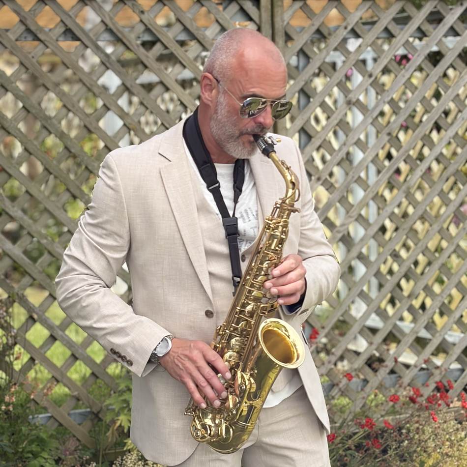 Paul Martyn playing saxophone in a smart suit, garden venue